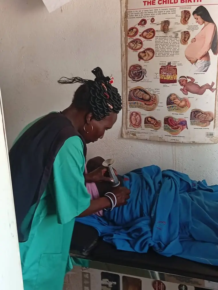 A midwife in green scrubs listening for a fetal heartbeat with a Pinard horn
